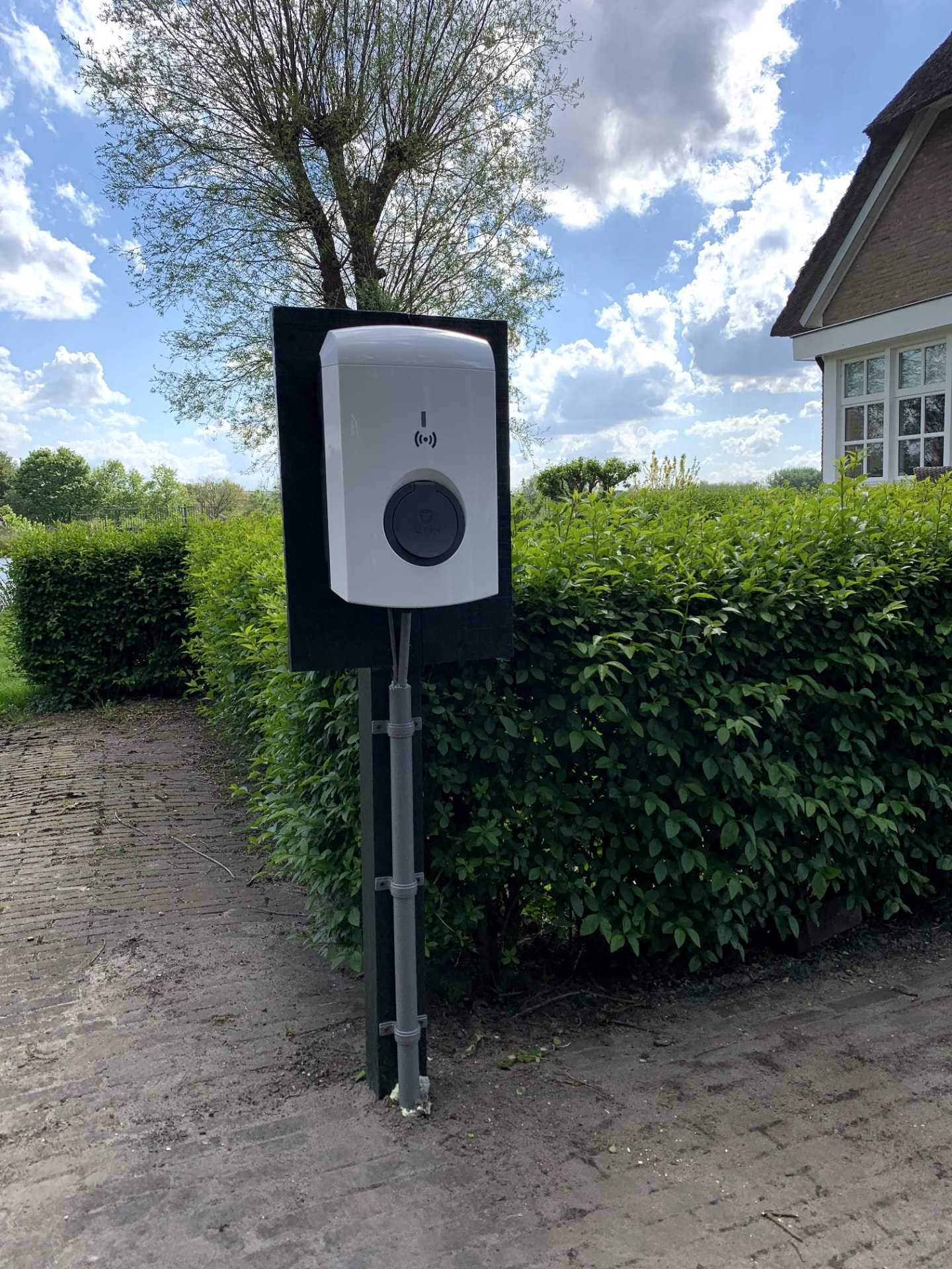 Laadpaal in de voortuin van een woning, netjes op een paal gemonteerd